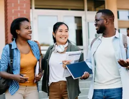 three friends holding notebooks outside of a school building